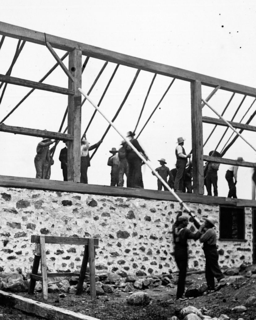 Men raising the timber frame of a barn on a stone foundation in Ontario, around 1905.